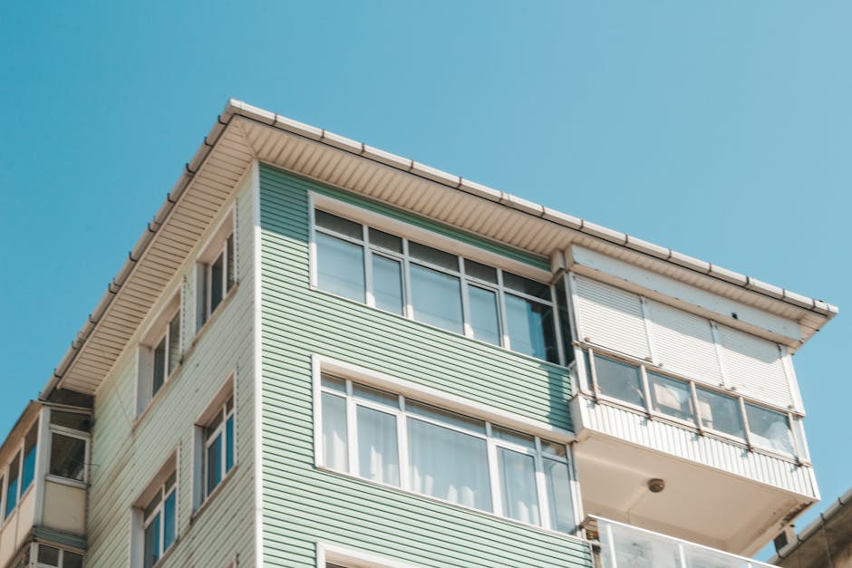 Low angle view of a modern apartment building exterior with glass windows under a clear blue sky